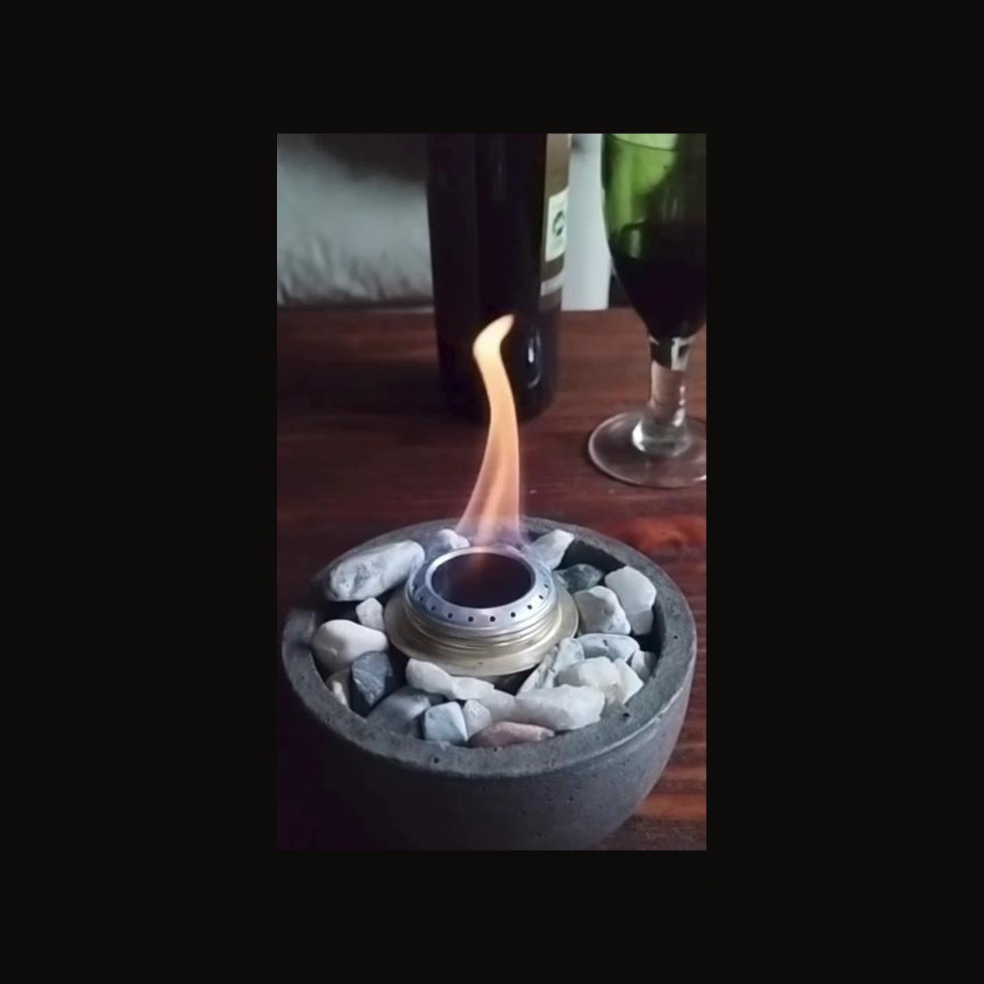 Fogón decorativo de concreto con piedras y llama encendida sobre mesa de madera